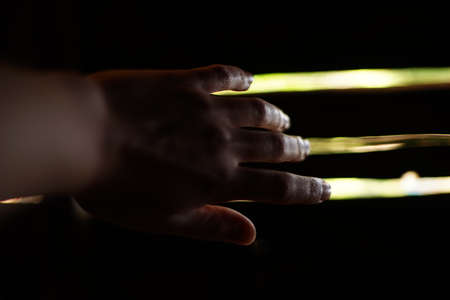 A close-up of a female hand reaching towards a door. It is dark and the only light is coming through the cracks of the door.の写真素材