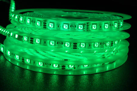 From above bobbins with three roll of glowing LED strip lighting, color green, placed on table in dim room.の写真素材