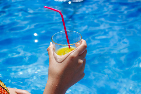 Unrecognizable person with transparent glass of fresh cold orange juice with ice and red straw...