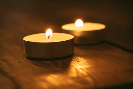 Tea light candles lit with flame placed on wooden table in dark room