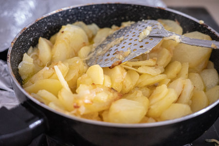 Spanish omelette preparation with sliced potatoes frying in a panの写真素材