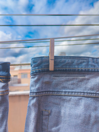 Blue denim jeans hanging on a clothesline with wooden clothespin outdoorsの写真素材