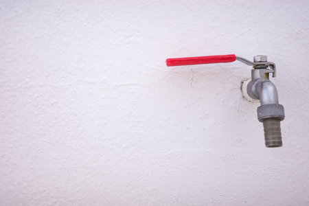 Outdoor metal faucet with red handle on white wallの写真素材
