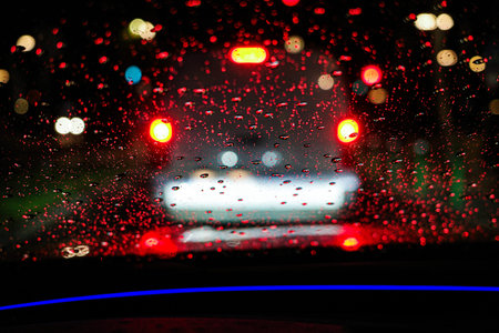 Night traffic through rainy car windshield with blurred lights