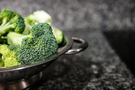 Fresh broccoli in a metal colander on kitchen counter