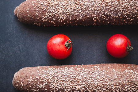 Whole wheat bread with sesame seeds and fresh cherry tomatoes on dark backgroundの写真素材