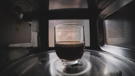 Cup of coffee heating inside microwave oven, interior view of kitchen appliance