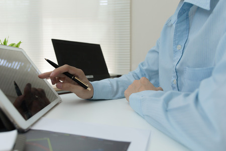 Business planning concept : Businessman with finger touching screen of a digital tablet at office on table with document graph data, Businessman looking about cost, budget or invesment data in tablet. Business planning concept : Businessman with finger touching screen of a digital tablet at office on table with document graph data, Businessman looking about cost, budget or invesment data in tablet.