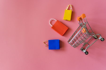 Minimal shoping online concept, Colorful paper shopping bag and trolley go down from floating pink background for copy space. Customer can buy everthing form home and the messenger will deliver.の写真素材