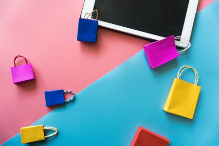 Minimal shoping online concept, Colorful paper shopping bag and trolley go down from floating pink background for copy space. Customer can buy everthing form home and the messenger will deliver.の写真素材