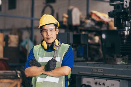 Portrait of industrial engineer wearing a yellow helmet while standing in a heavy industrial factory behindの写真素材
