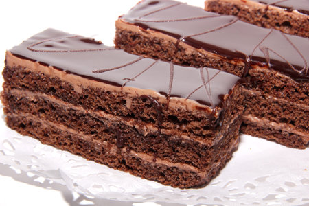 Three chocolate cake with cream and chocolate glaze on a lace napkin
