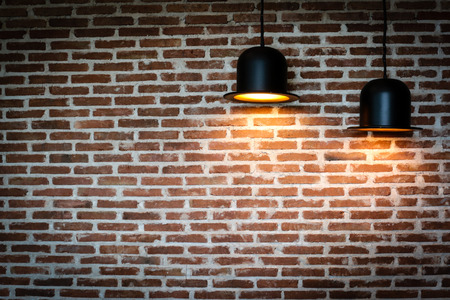 Black lamps is shining orange light on red brick wall for background texture.の写真素材
