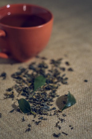Dry tea with green leaves in cup, on burlap background.の写真素材