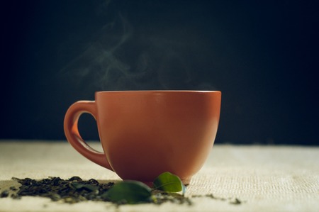 Dry tea with green leaves in cup, on burlap background.の写真素材
