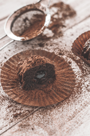 Chocolate chip muffin in brown wax paper. Unwrapped. Cocoa powder in the backgroundの写真素材
