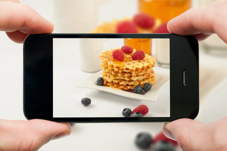 Taking photo of waffles by smartphone. Closeup view of process. File contains clipping paths for smartphone and hands and picture on itの写真素材