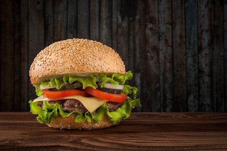 Delicious cheeseburger with salad ingredients on a grilled beef patty on a rustic wooden table with copyspace.の写真素材