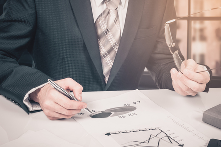 business documents on office table with laptop computer and graph financial digital diagram and businessman working in the backgroundの写真素材