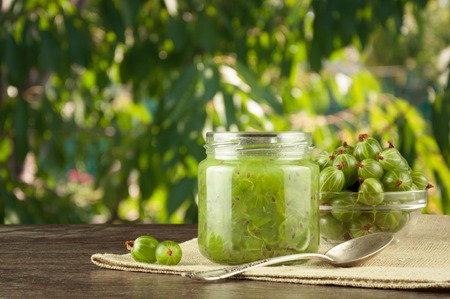 Gooseberry smoothie in a jar on a brown table and background of green leaves.の写真素材