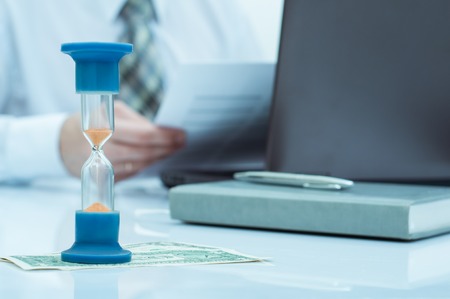 Hourglass. Businessman working in the office in the background. Concept time is moneyの写真素材