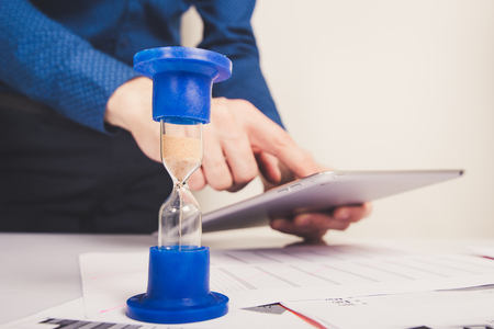 Hourglass. Businessman working in the office in the background. Concept time is money.の写真素材