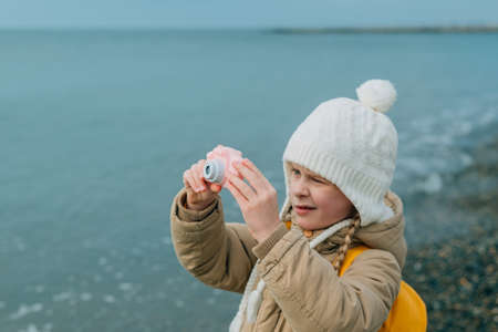 a little girl squinting photographs the autumn seascape on a childrens pink camera. the child is passionately engaged in his hobby: photographyの写真素材