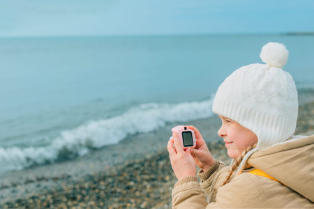a little girl squinting photographs the autumn, spring seascape on a childrens pink camera. the...