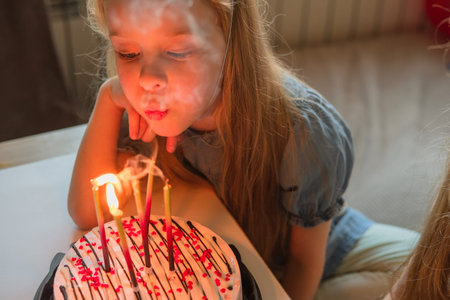 little girls, sisters, twins happily blew out the candles on the birthday cake at home festive cap....