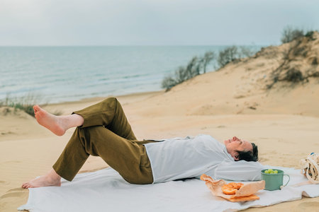 adult woman in the spring at a picnic on the beach by the sea lies on plaid with a smile, enjoymentの写真素材
