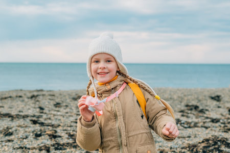 little cheerful girl with a smile shows the screen of a childrens pink camera in autumn on the sea....