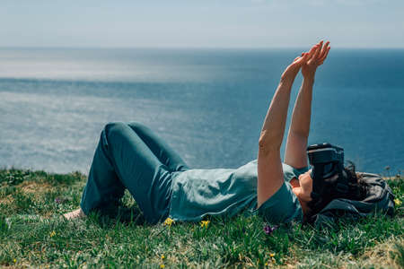 an adult woman lies on a mountain against the background of the sea in summer, spring in virtual reality glasses. VRの写真素材