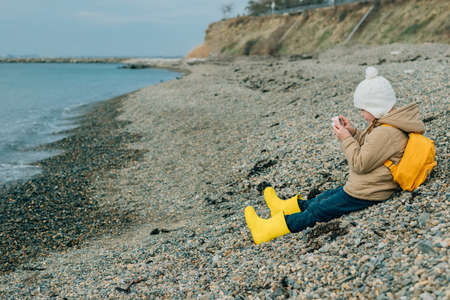 little girl looks at the screen of a childrens pink camera to see her photos of the autumn, spring seascape. the child is passionate about his hobby: photographyの写真素材