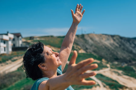 close-up portrait of an adult woman on a mountain with a smile on her face, raising her hands to the sky and the sun on a sunny day having fun on the background of the ocean in springの写真素材