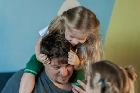 twin daughters are trying to divide their father, childish jealousy. Dad playing at home with childrenの写真素材