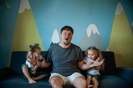 twin daughters are trying to divide their father, childish jealousy. Dad playing at home with childrenの写真素材