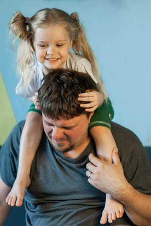 daughter plays with dad, crawling over him, climbing onto his neck at homeの写真素材