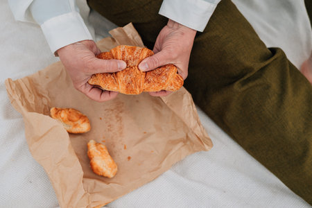 close-up. An adult woman holds a fresh croissant in her hands. Outdoor breakfast