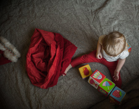 child, kid peeks into the red bag of santa claus at home, sitting on the bed to find gifts. Christmas moodの写真素材
