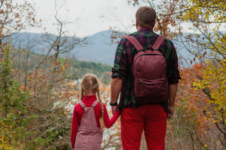 little girl daughter goes with dad on a hike in the autumn forest. back viewの写真素材
