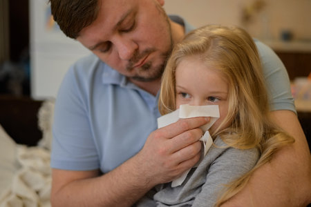 dad wipes his sick childs nose with a white disposable paper napkin at home. The father suspects that his daughter is ill. The child is not feeling well. the concept of equality in the family between father and mother. Father on sick leave with child at homeの写真素材
