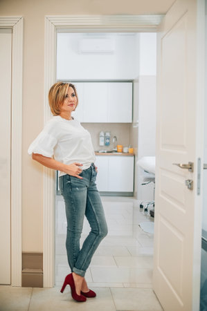 portrait of a beautiful slender woman in full growth in the doorway of a bright medical office. the proprietress of the cosmetology clinic with a smile on her face stands at the entrance to the doctors officeの写真素材