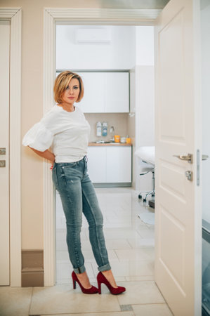 portrait of a beautiful slender woman in full growth in the doorway of a bright medical office. the proprietress of the cosmetology clinic with a smile on her face stands at the entrance to the doctors officeの写真素材