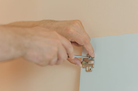 a man tightens a screw with a screwdriver in a door hinge on a white cabinet door