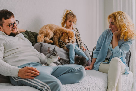 happy friendly family sits at home on the couch, having fun, laughing. Parents play with their children and pets. Dad, teenage son, little daughter, mom, a red poodle.の写真素材