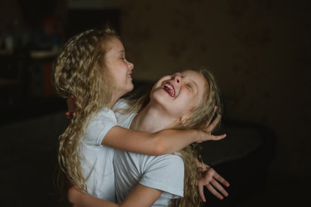 two little girls with curly long hair fooling around at homeの写真素材