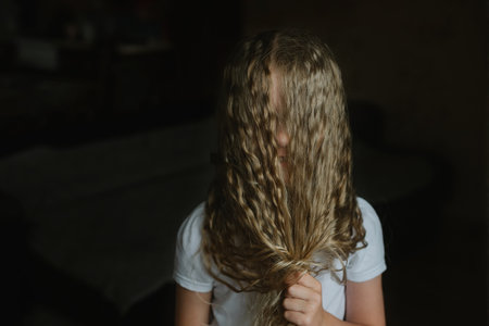 little girl covers her face with her long curly hair, shyness, funの写真素材
