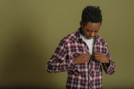 young man african american man buttoning up plaid shirtの写真素材