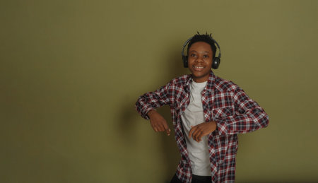Young african american guy listens to music on headphones and dances on a green backgroundの写真素材