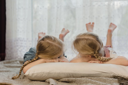 two little girls sisters lie on their stomachs on the floor at home and smileの写真素材